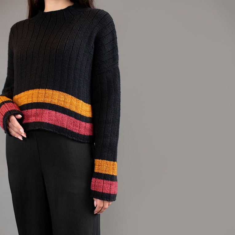 Torso of a woman wearing a black sweater with pink and amber stripes at the cuffs and hem.
