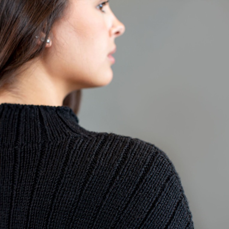 Close up of the shoulder and neck of a black, ribbed sweater.