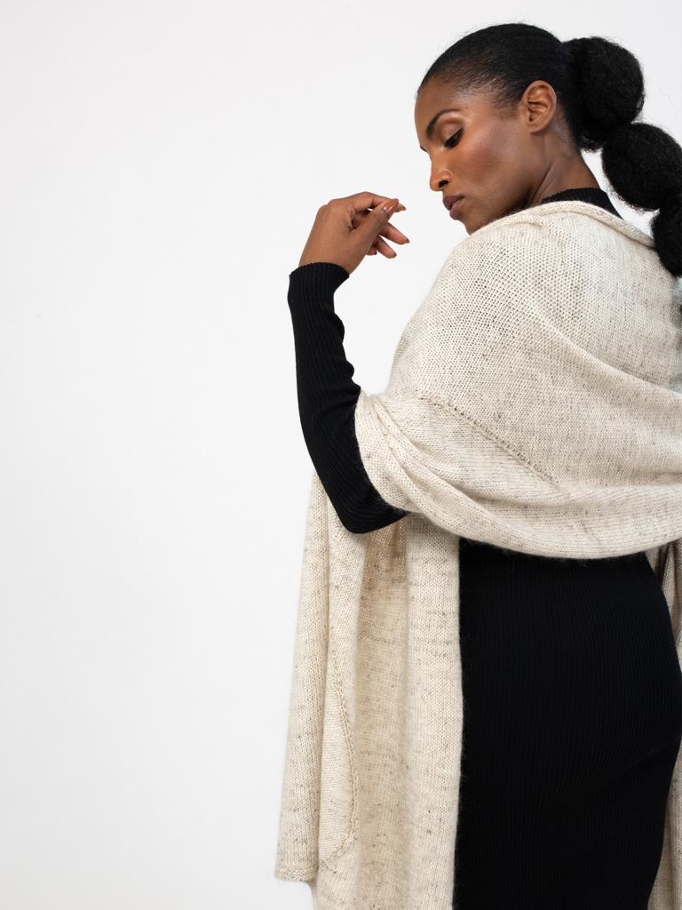A woman seen from the back, wrapped in Departure Bay: a hand knit shawl worked in stockinette and reverse stockinette, each section separated by a deep, wavy line.